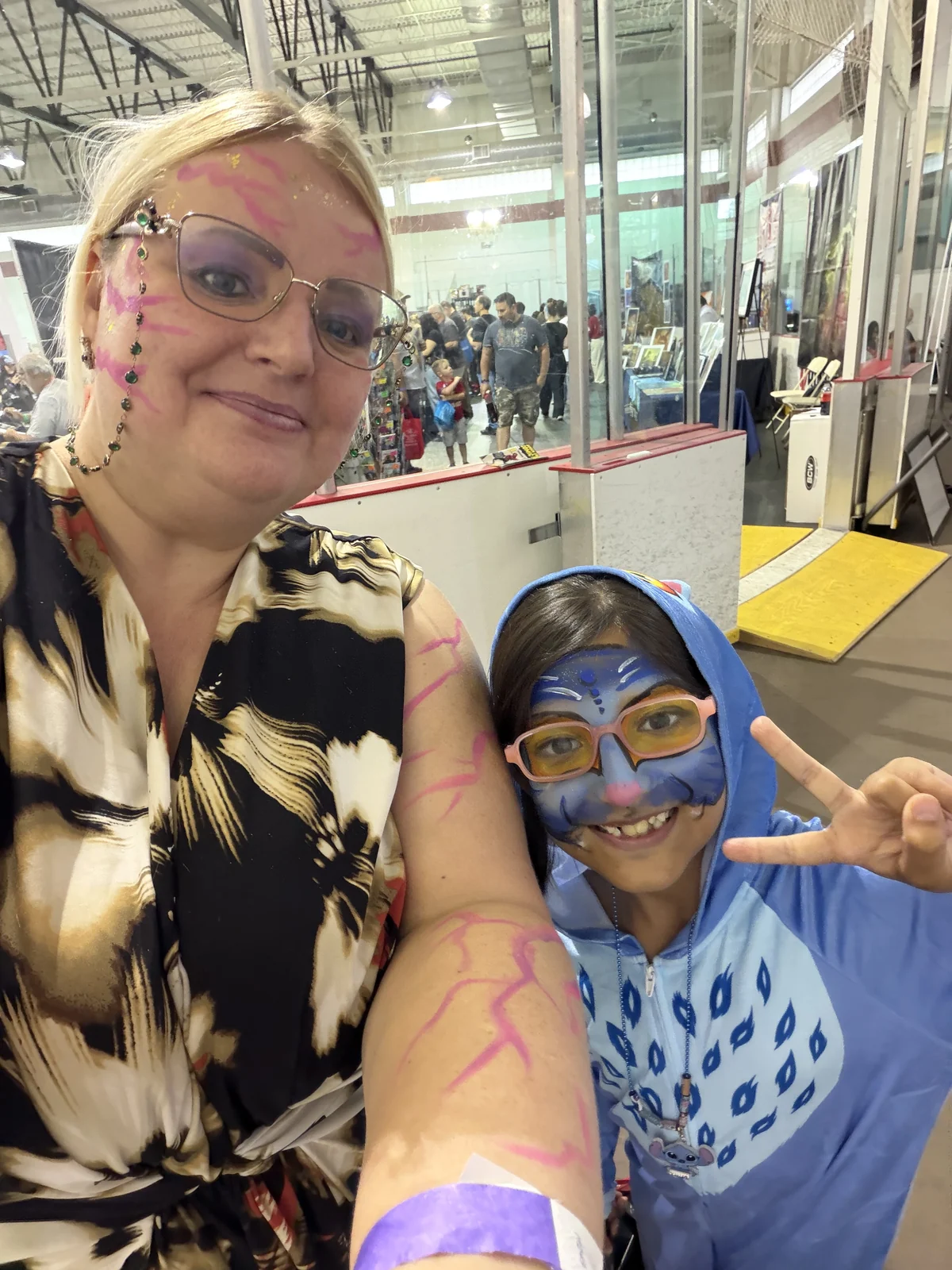 Julie with pink face paint beside a smiling child wearing blue face paint and a blue costume at an indoor event