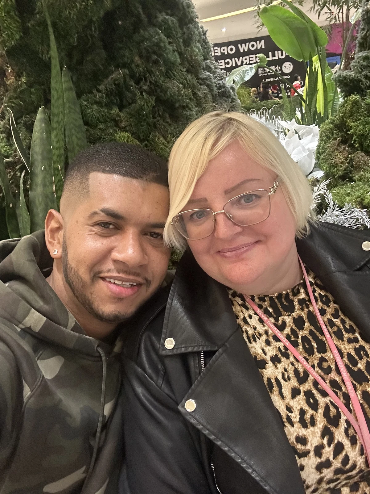 Julie smiling with a companion in front of a green plant display