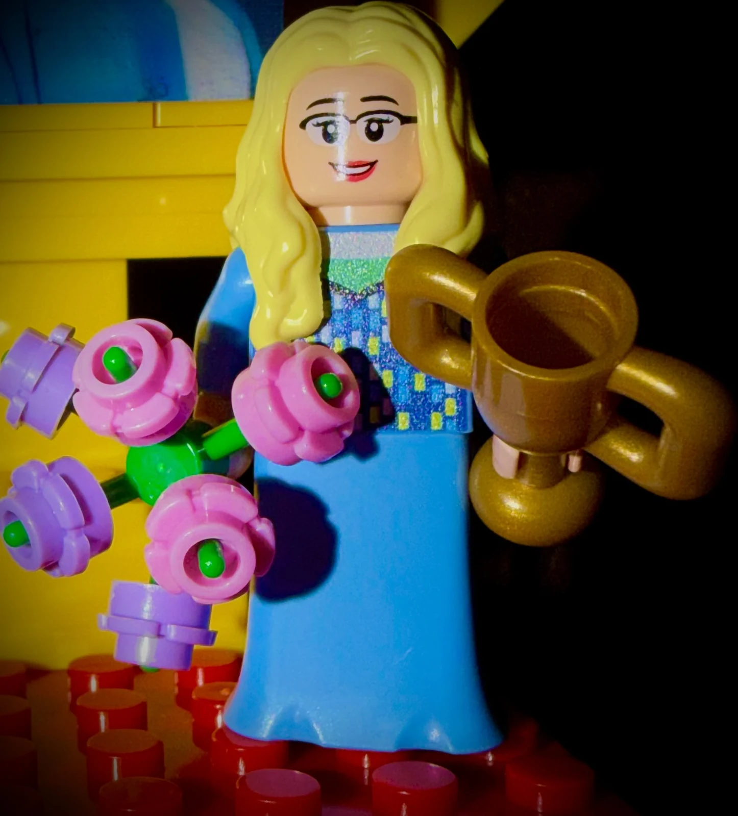 Close view of the smiling LEGO Julie minifigure holding flowers and a gold trophy